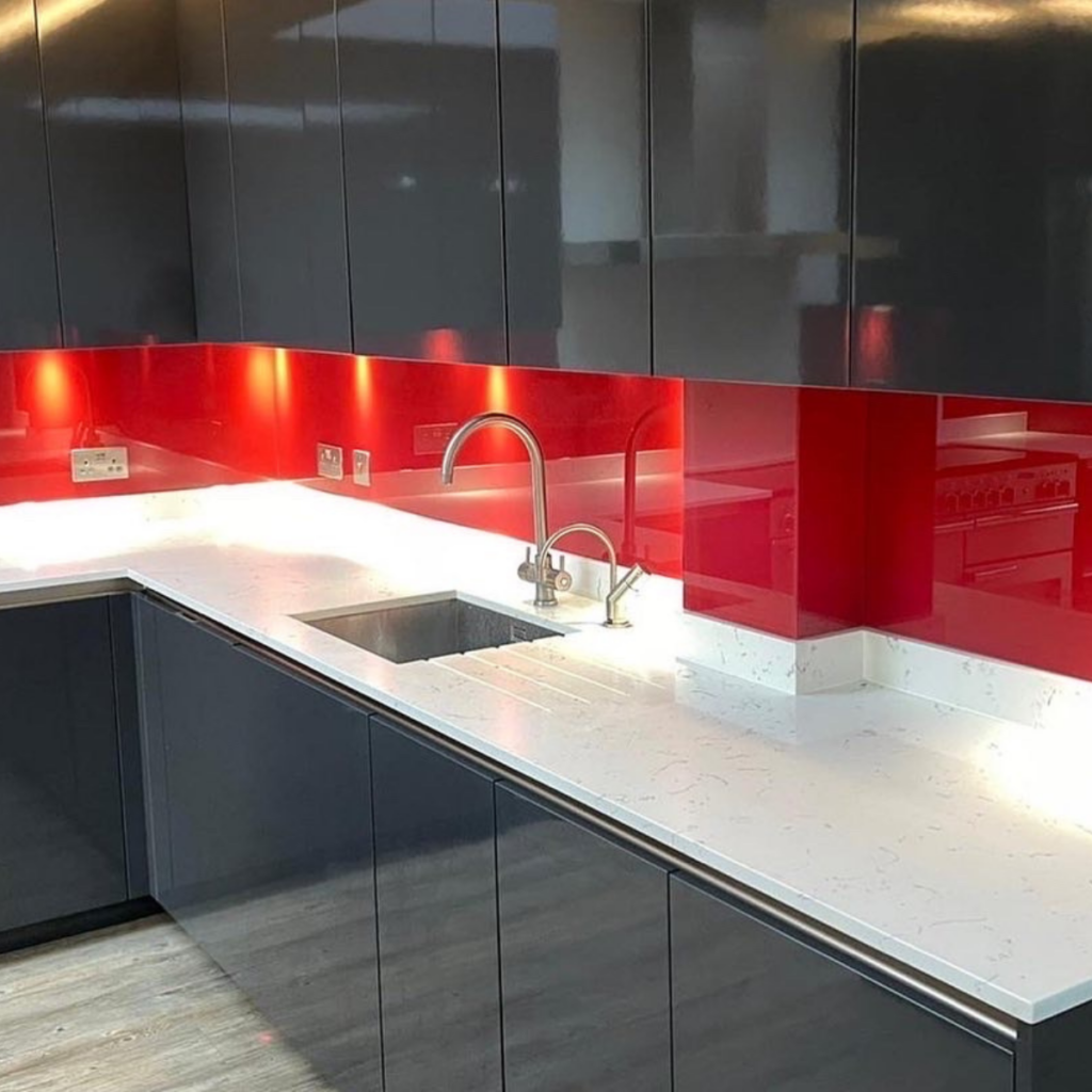 red painted glass splashbacks in a kitchen with dark grey cabinets and white worktops.